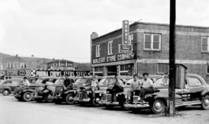 Getting around Spruce Pine in the 1940s was made easier by a fleet of taxis shown in this Jim Jones photograph. Their lineups on Upper Street are a poignant view of an earlier time. Above, pictured (R-L) are Pete Ellis, Plug Pittman, Ernest King, Lawrence Smith, Mutt Burleson, and Howard Hise in front Burleson Store. Note the phone box on the pole beside the cars that was their office.